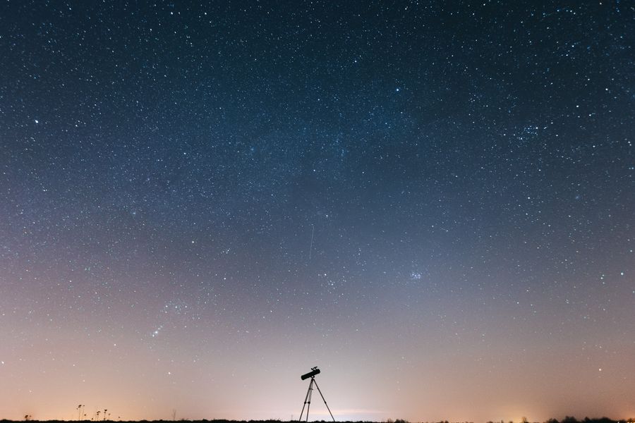 Silhouette of a person using a telescope under a star-filled night sky