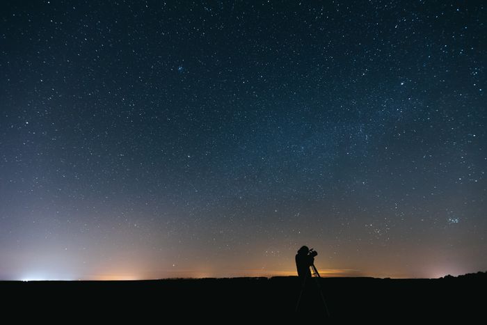 The silhouette of a person raising binoculars to a starry sky above a low horizon
