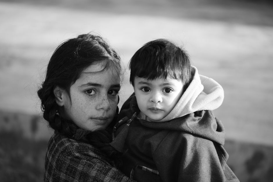 Heartfelt black and white portrait of siblings, an older girl holding a young child outdoors, showcasing familial bond and innocence.