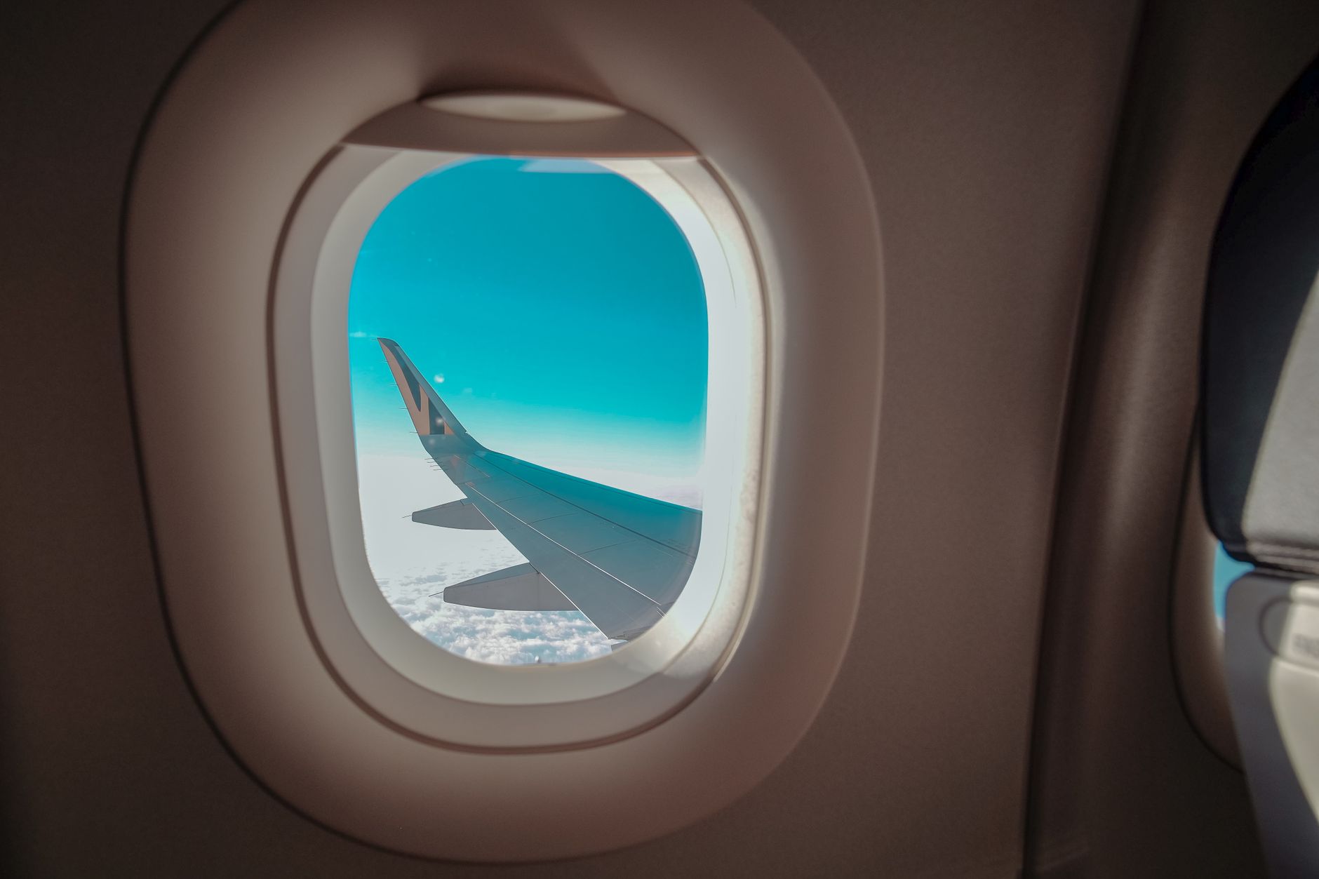 A stunning view of an airplane wing through a cabin window against a blue sky.