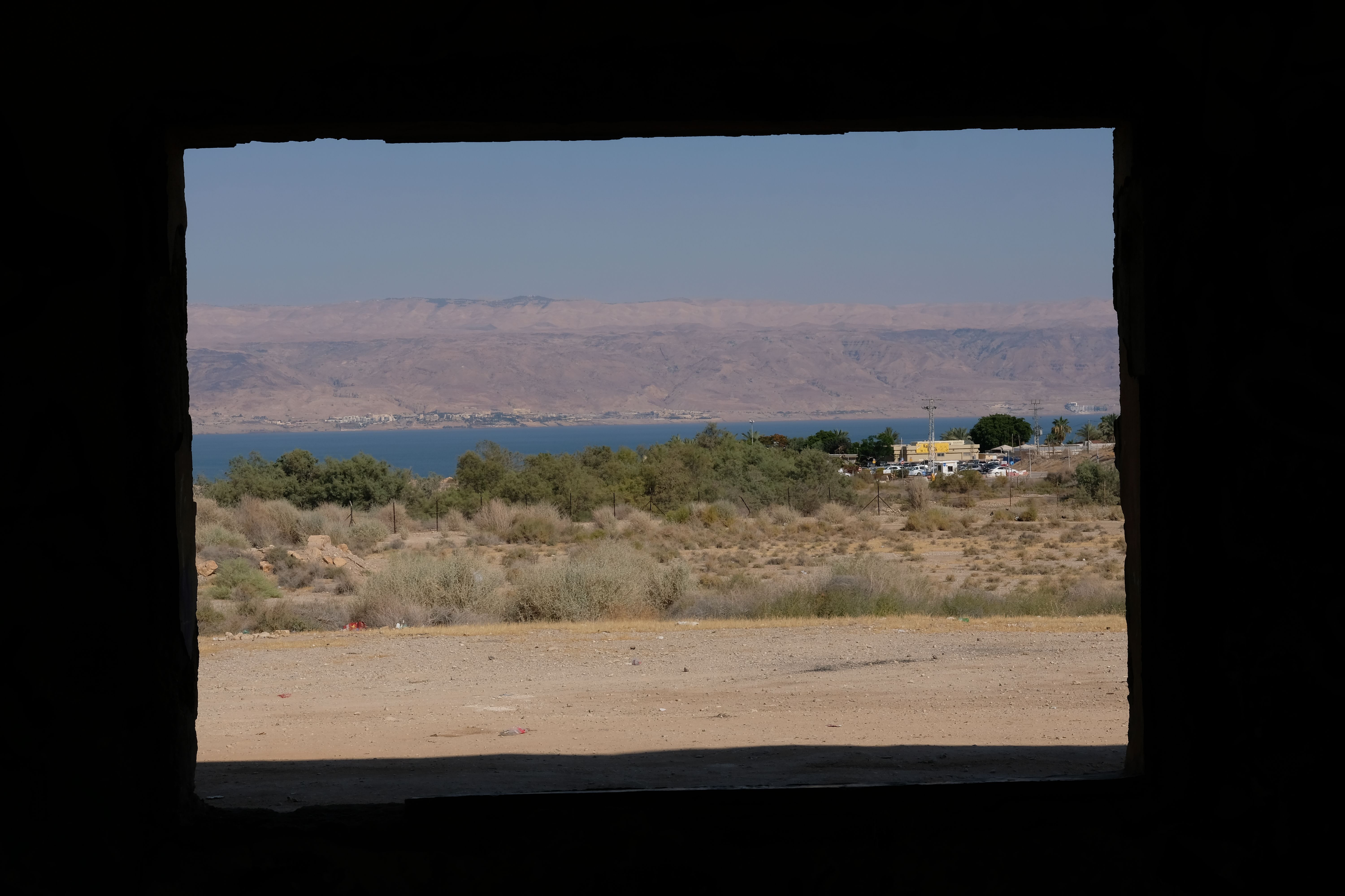 View through a window frame of a desert landscape meeting a body of water.