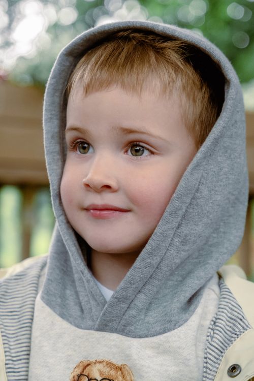 Free Adorable young boy in a grey hoodie smiling, captured outdoors with natural light. Stock Photo