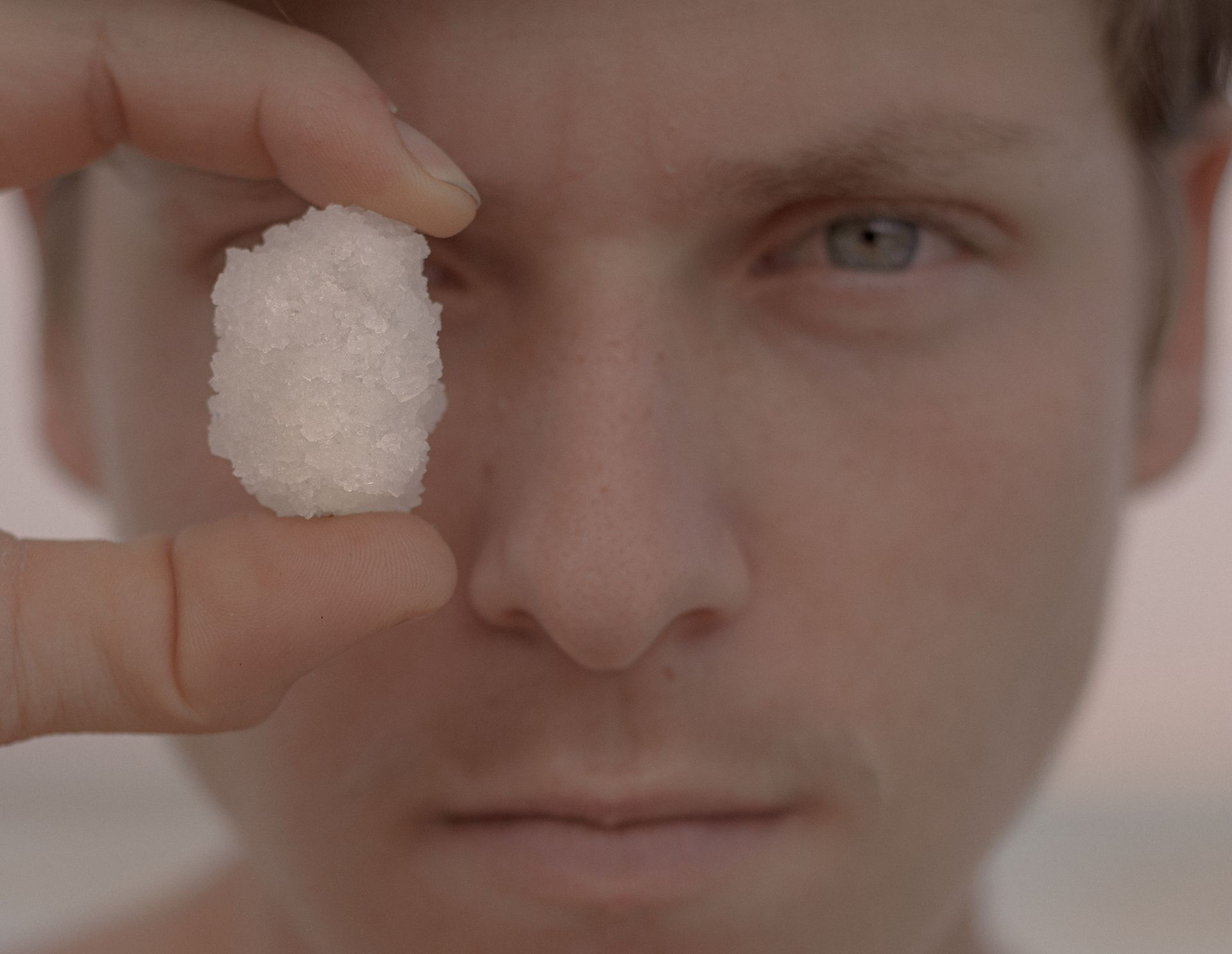 Close-up of a man holding a salt crystal near his eye, showing texture details.
