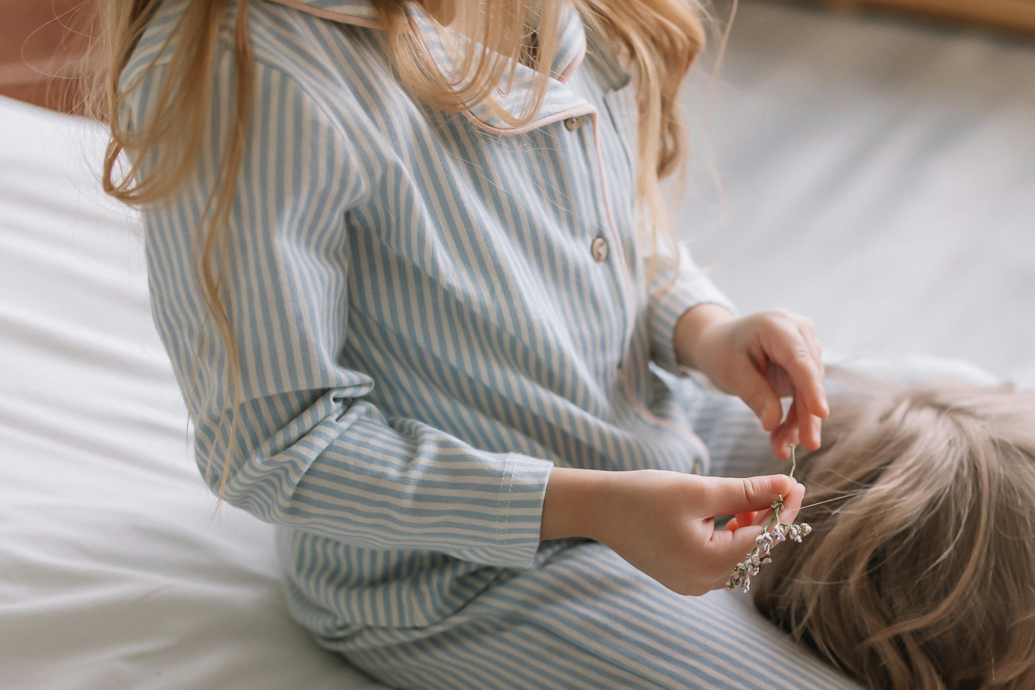 Child sitting on a bed in striped pajamas, holding flowers, exudes a calm morning vibe.