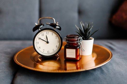 Aesthetic arrangement of a clock and jar on a golden tray with a potted plant.