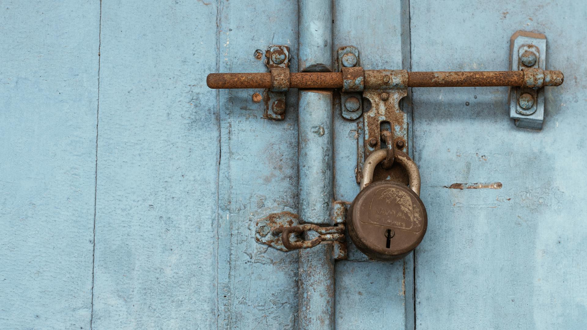 Close-up of an old rusty padlock securing a wooden blue door for safety.