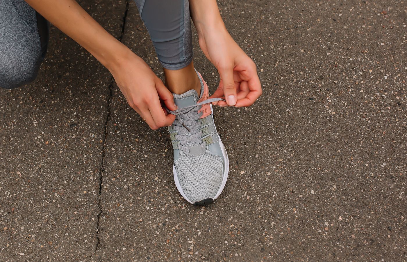 Close-up image of a person tying shoelaces on a sneaker while sitting on pavement.
