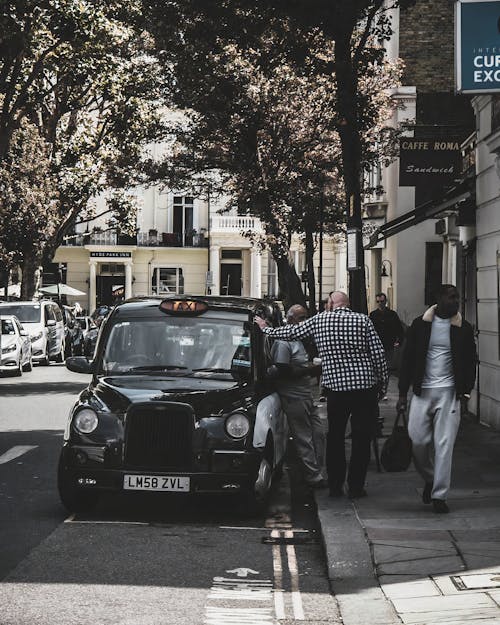 Free People Standing on Sidewalk Near Black Taxi Stock Photo