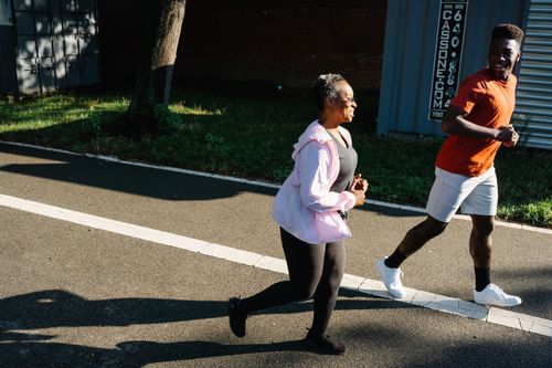 Free Two adults jogging outdoors on a sunny day, embracing a healthy lifestyle with smiles. Stock Photo