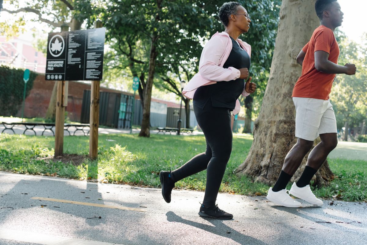 Young man and elderly woman jogging together in a park on a sunny day