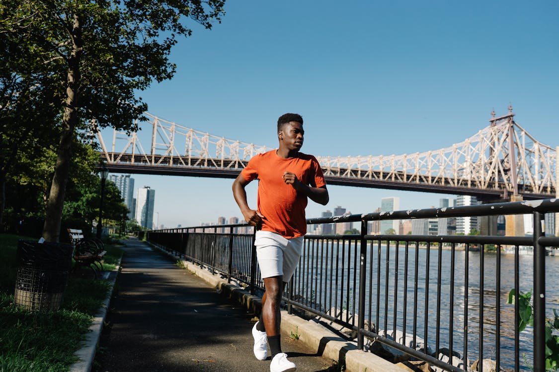 Man Wearing Orange T-shirt and White Shorts Running Near a Bridge