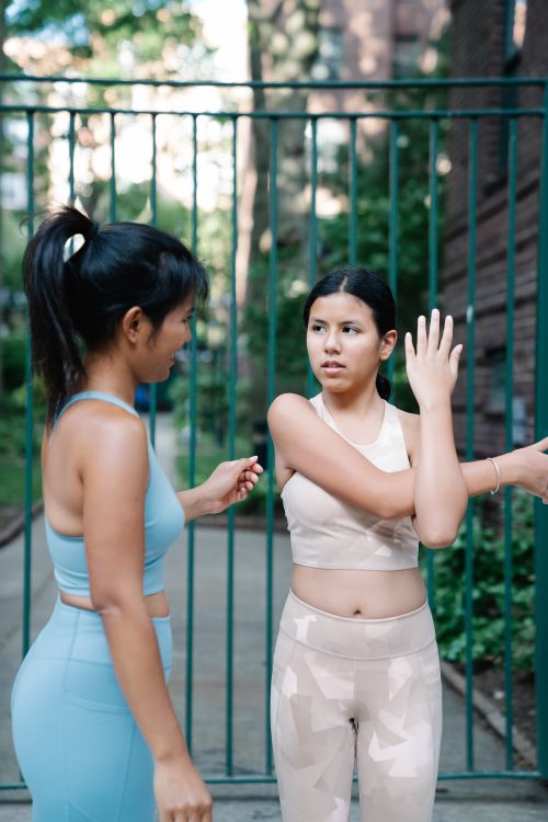 Free Two young women stretching in sportswear outdoors, enjoying a summer workout session together. Stock Photo