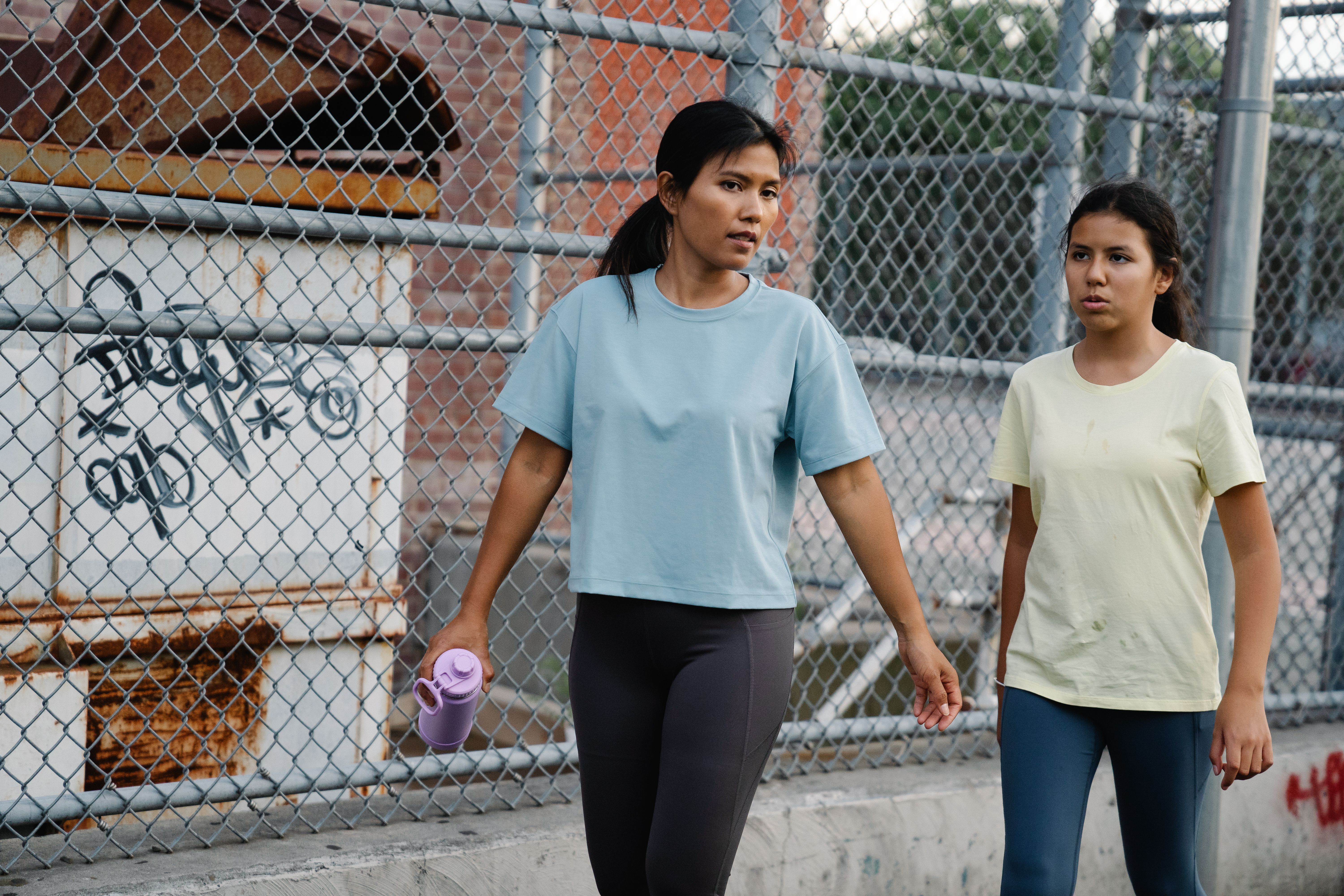 Mother and daughter exercising outdoors on an urban pathway, promoting healthy lifestyle.