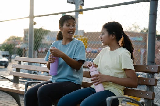 Two women enjoying a relaxed conversation outdoors with water bottles on a park bench.