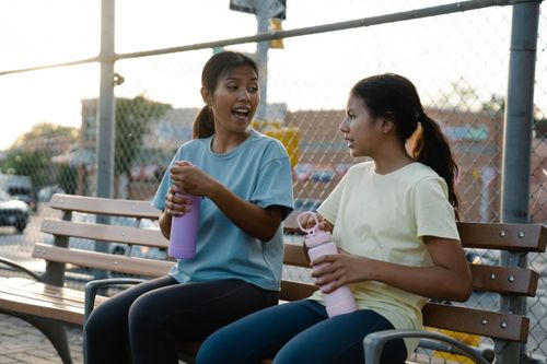 Free Two women enjoying a relaxed conversation outdoors with water bottles on a park bench. Stock Photo