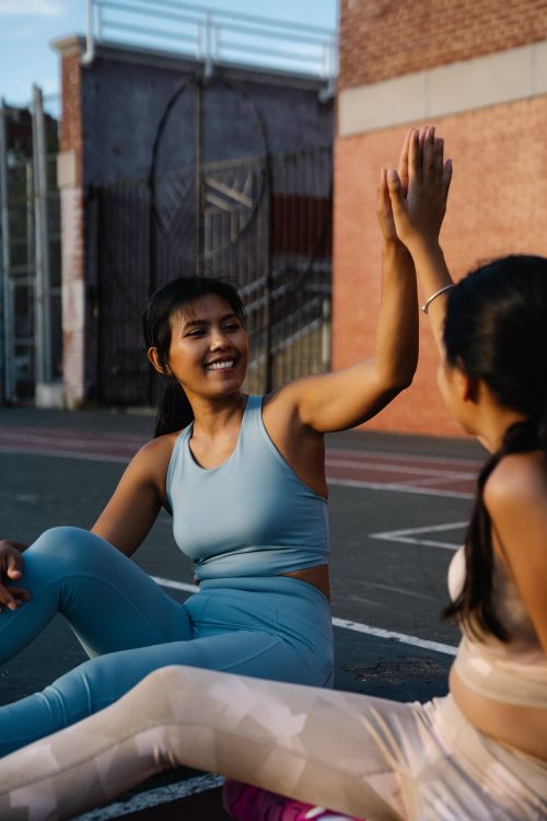 Free Two women in activewear sharing a spirited high five at an outdoor sports court. Stock Photo