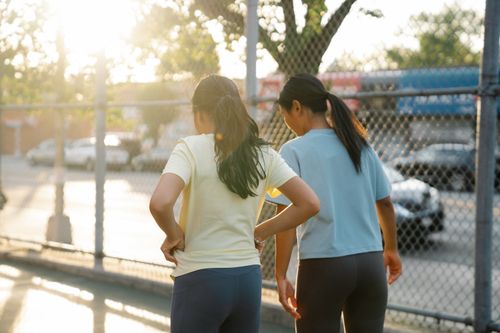 Free Back view of two women exercising near a chain-link fence on a sunny day. Stock Photo