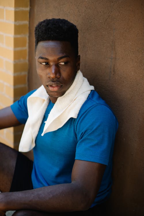 A Man in  Blue Shirt Leaning on Brown Wall while Looking Afar