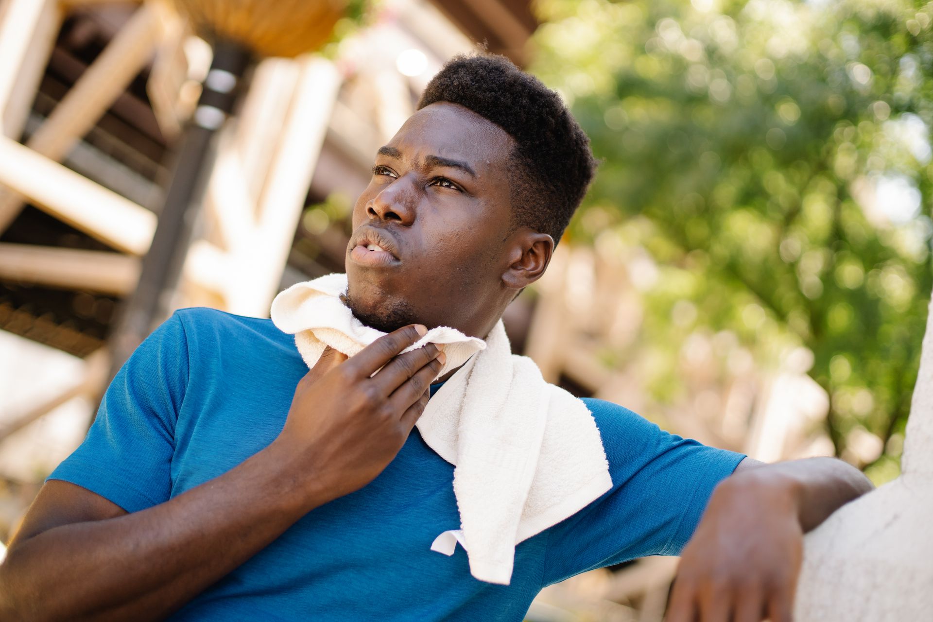 A man cooling down with a towel on a bright day, looking thoughtful outdoors.
