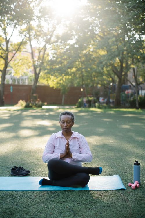 Free Senior woman practicing yoga meditation on a mat in a sunlit park. Stock Photo