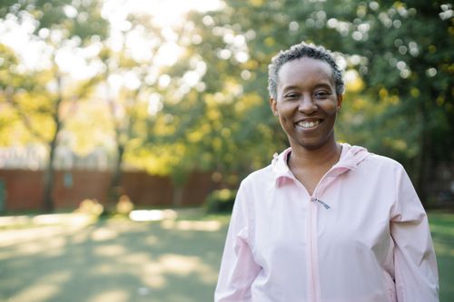Free Smiling woman in a pink jacket enjoying a sunny day in a park. Stock Photo