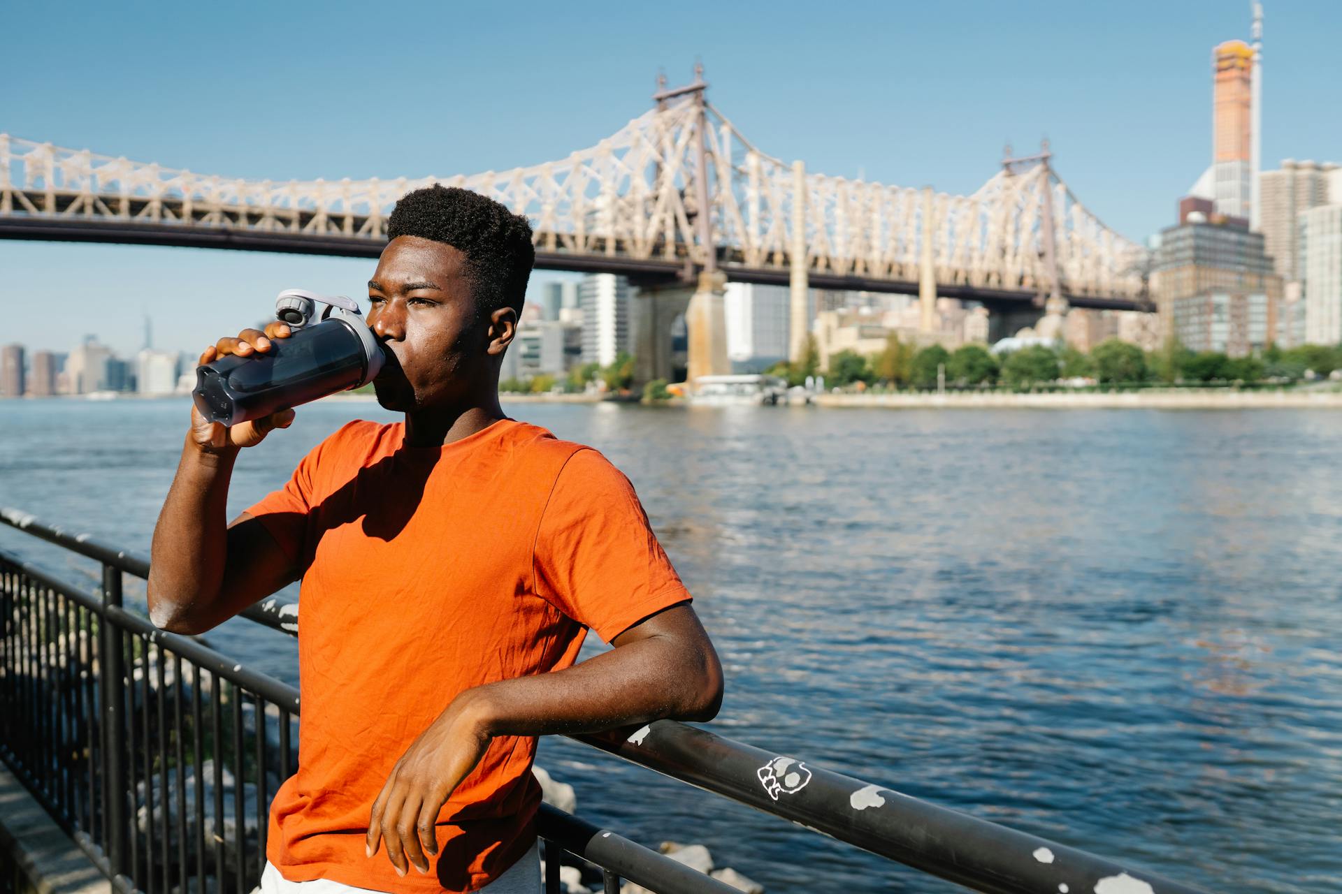 Man enjoying a drink by the East River with a bridge in the background. Perfect cityscape and lifestyle shot.