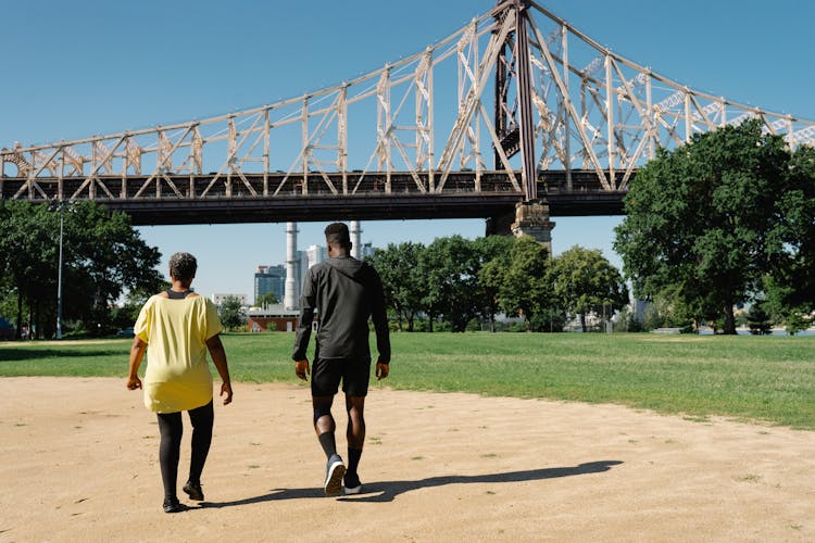 Back View Of People Walking On A Park Near A Bridge