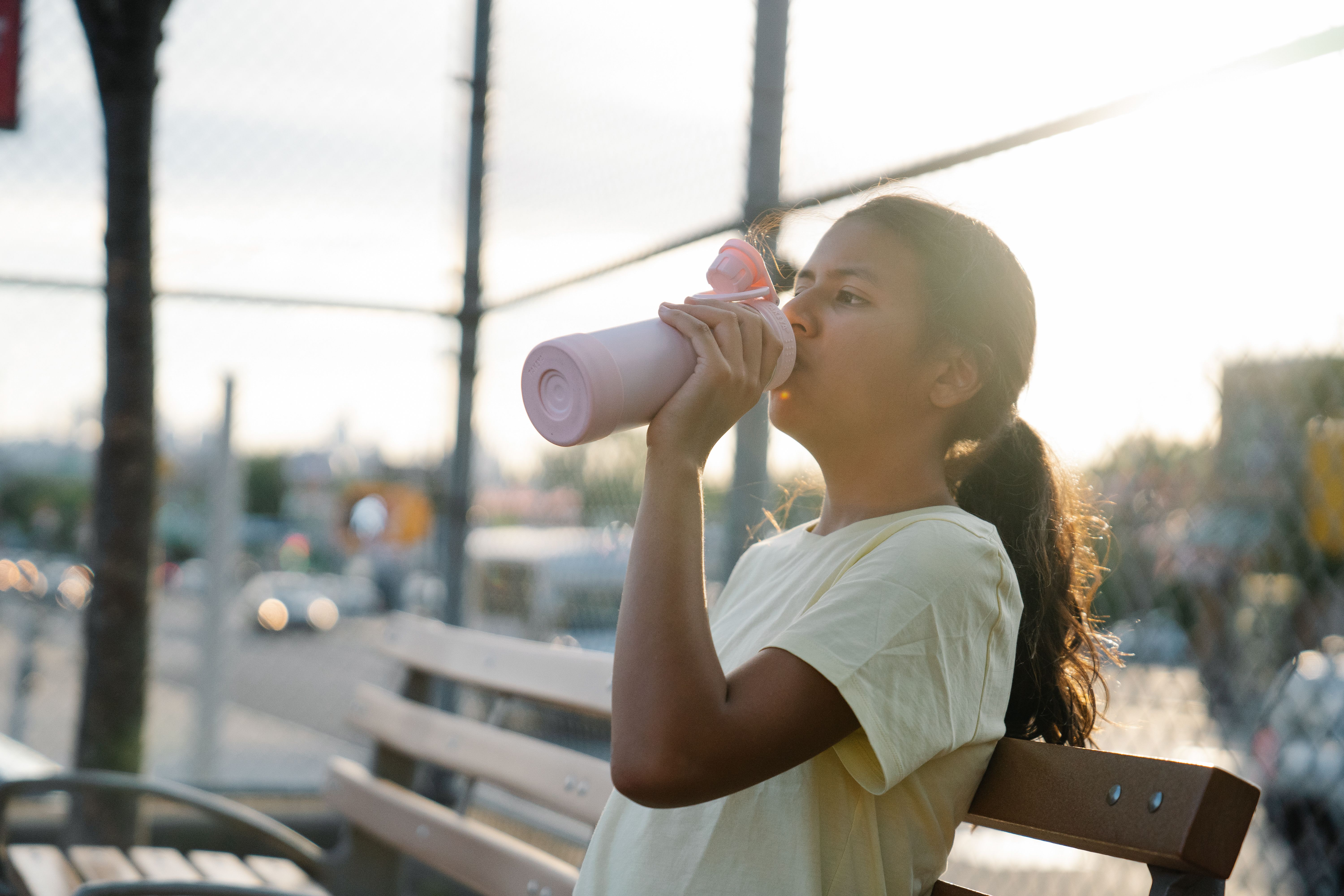 A child drinks water in the shade of a park on a summer afternoon.