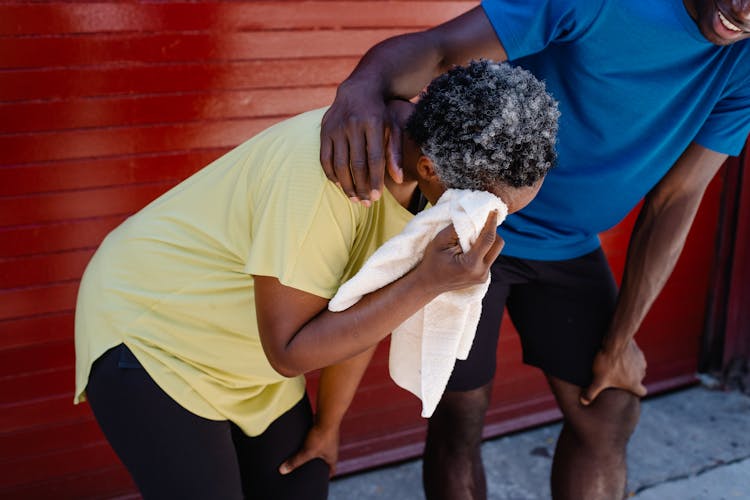 Man In Blue Shirt Assisting The Woman In Yellow Shirt While Wiping Her Sweat