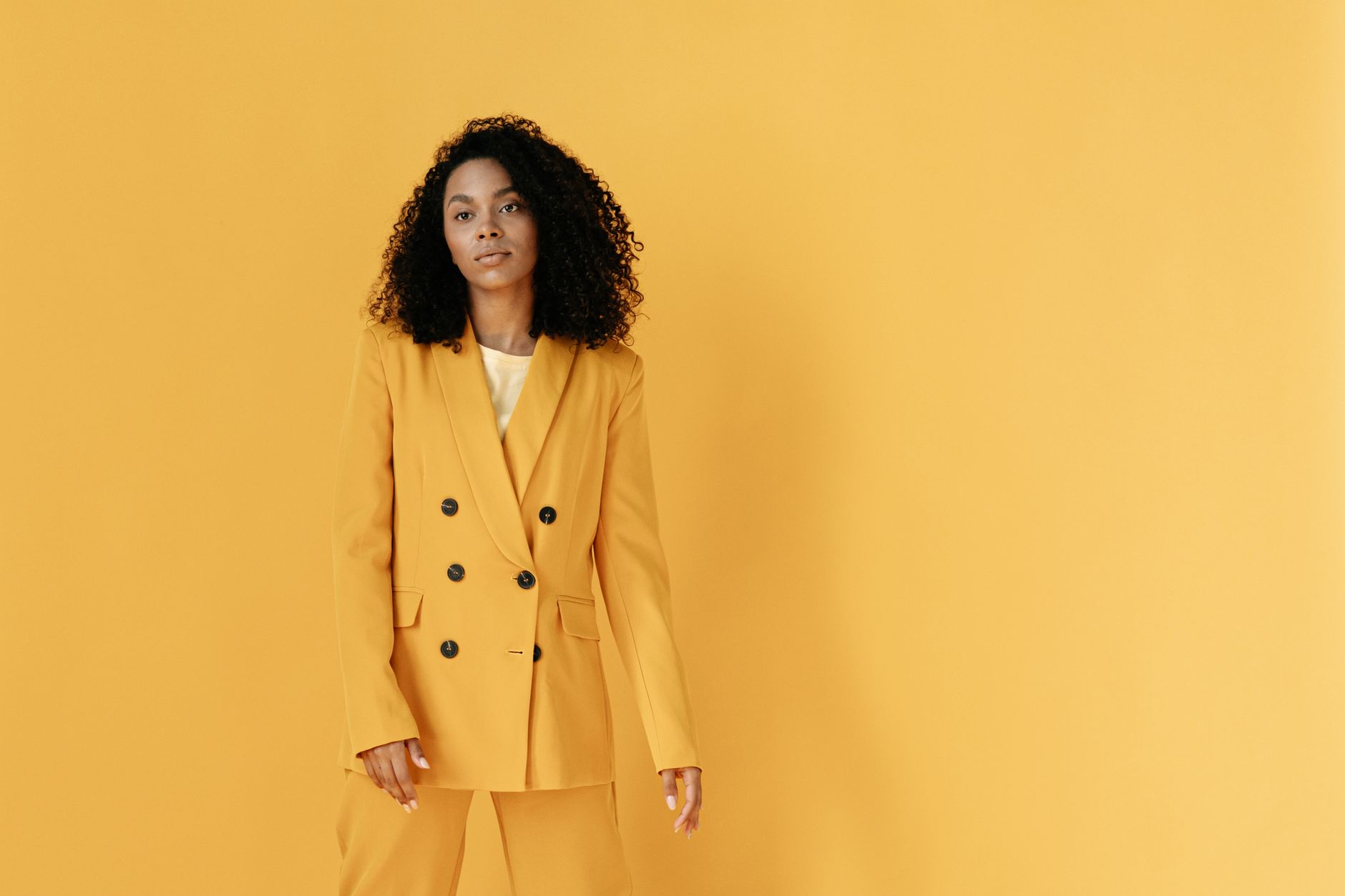 Confident black woman in a vibrant yellow suit posing against a matching background.