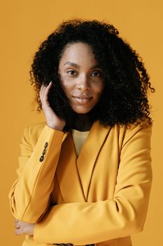 Striking portrait of a woman with afro hair wearing a yellow blazer against a yellow background.