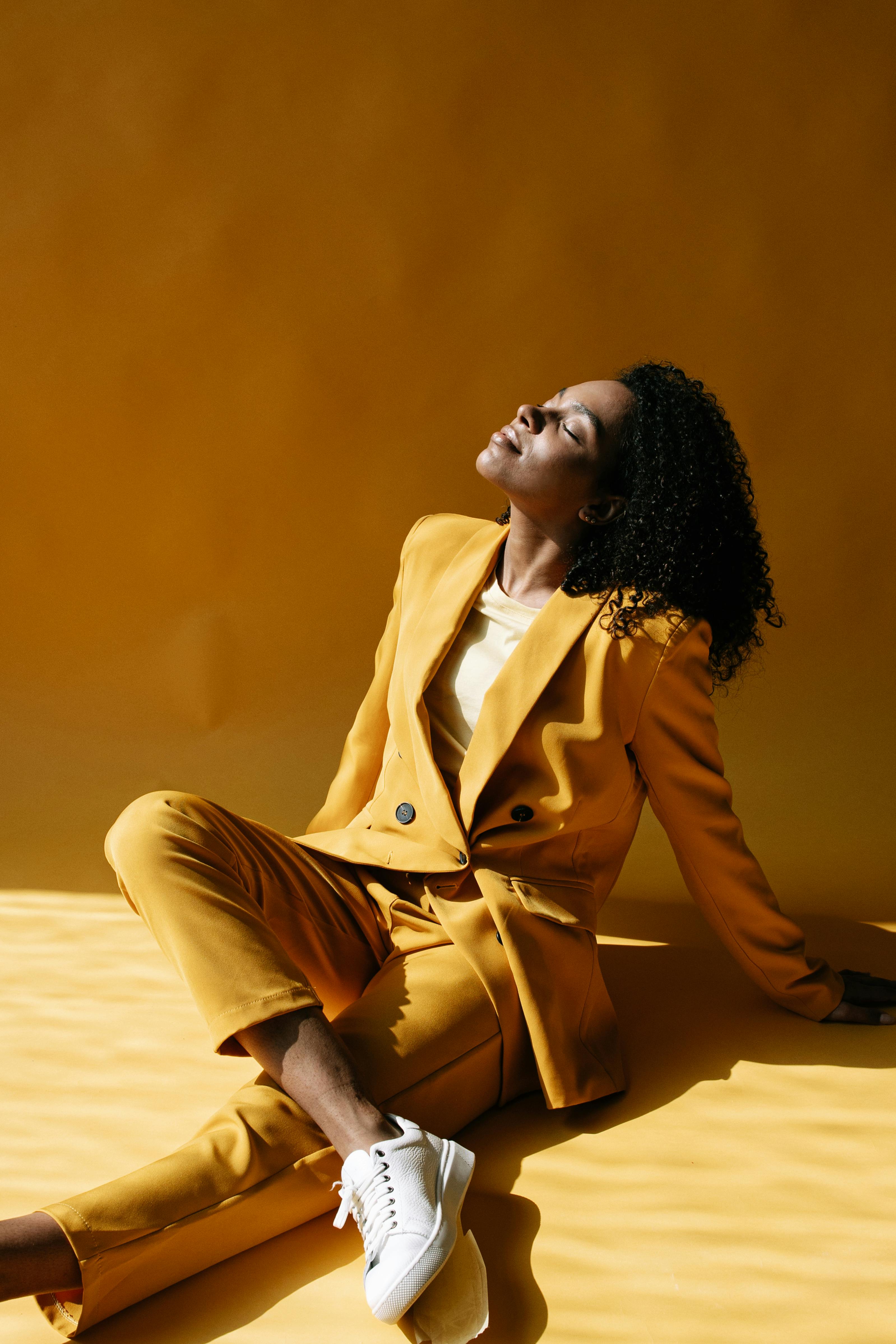 一位穿着黄色西装的时尚女士在充满活力的黄色背景下沐浴在阳光下