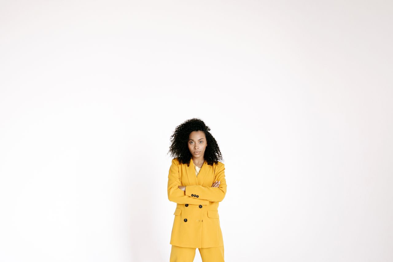 portrait of a confident woman in a yellow suit with curly hair arms cr