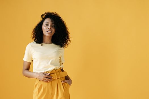 Stylish young woman in yellow fashion standing confidently against a vibrant backdrop.