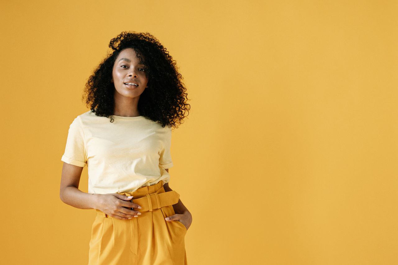 stylish young woman in yellow fashion standing confidently against a v