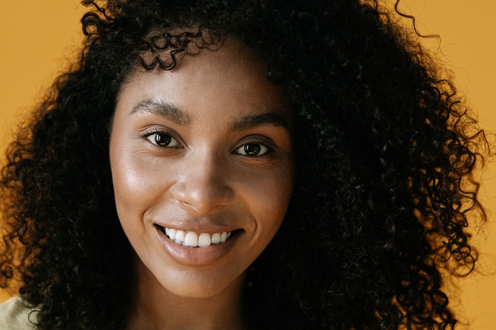 Close-up of a smiling woman with curly hair against a warm background.
