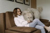 Woman in White Long Sleeve Shirt and Blue Denim Jeans Sitting on Brown Sofa