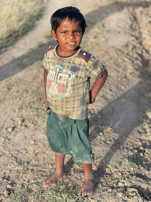 Free A cheerful young boy standing barefoot on a rural path, smiling at the camera. Stock Photo