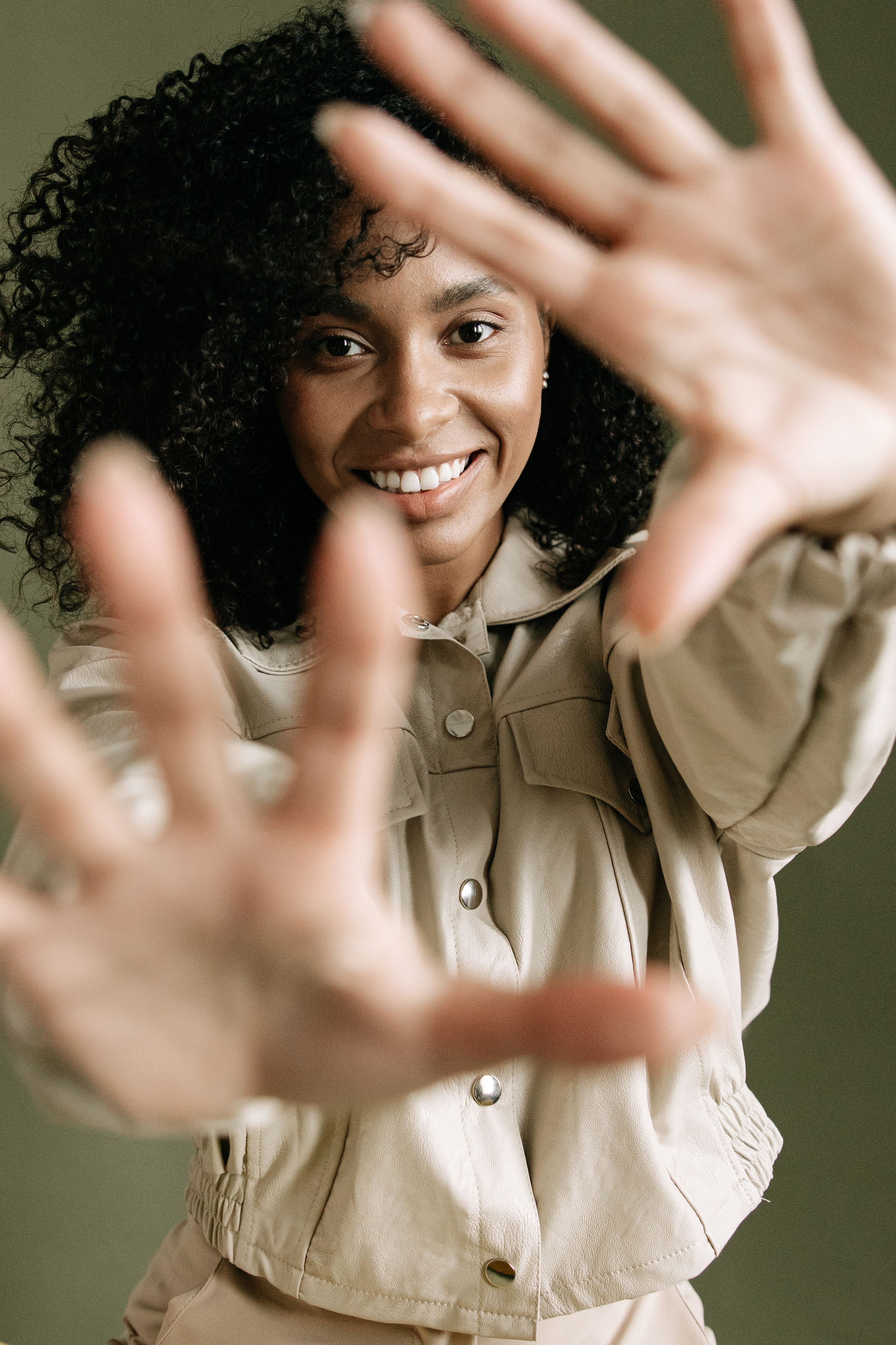 Portrait of a smiling woman with curly hair playfully reaching towards the camera, indoors.