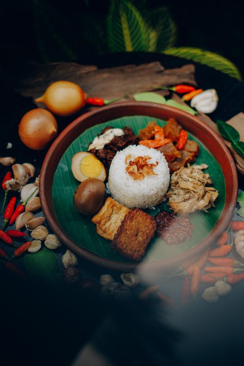 Free A delicious plate of Indonesian Nasi Campur served with rice, eggs, tempeh, and sambal, surrounded by fresh spices. Stock Photo