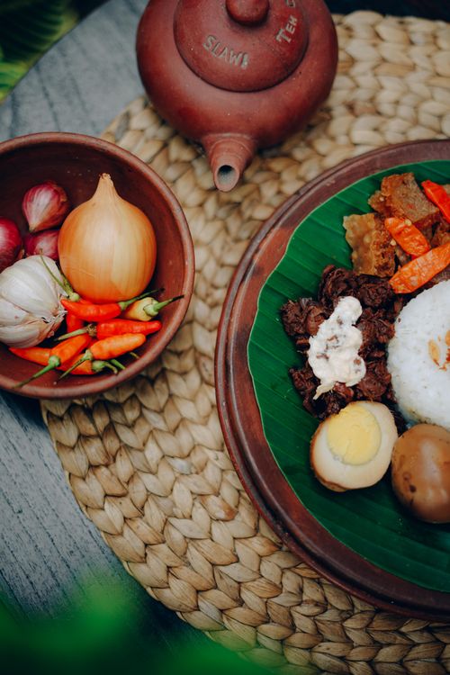 Free Top-down view of authentic Indonesian dishes with fresh ingredients and traditional teapot on woven mat. Stock Photo