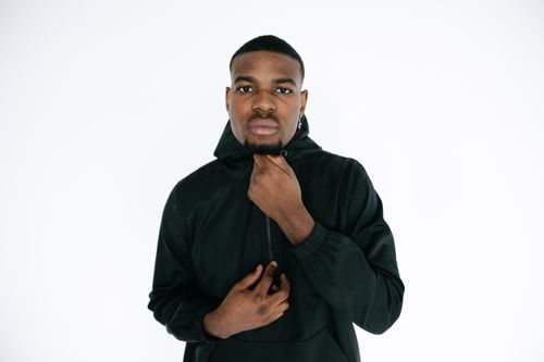 Free Studio portrait of a man in a black hooded jacket posing against a white background. Stock Photo