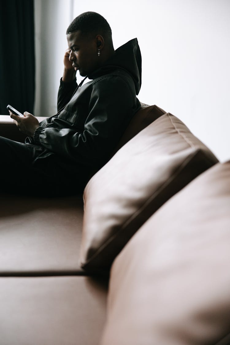 A Man Sitting On Sofa While Holding Cellphone