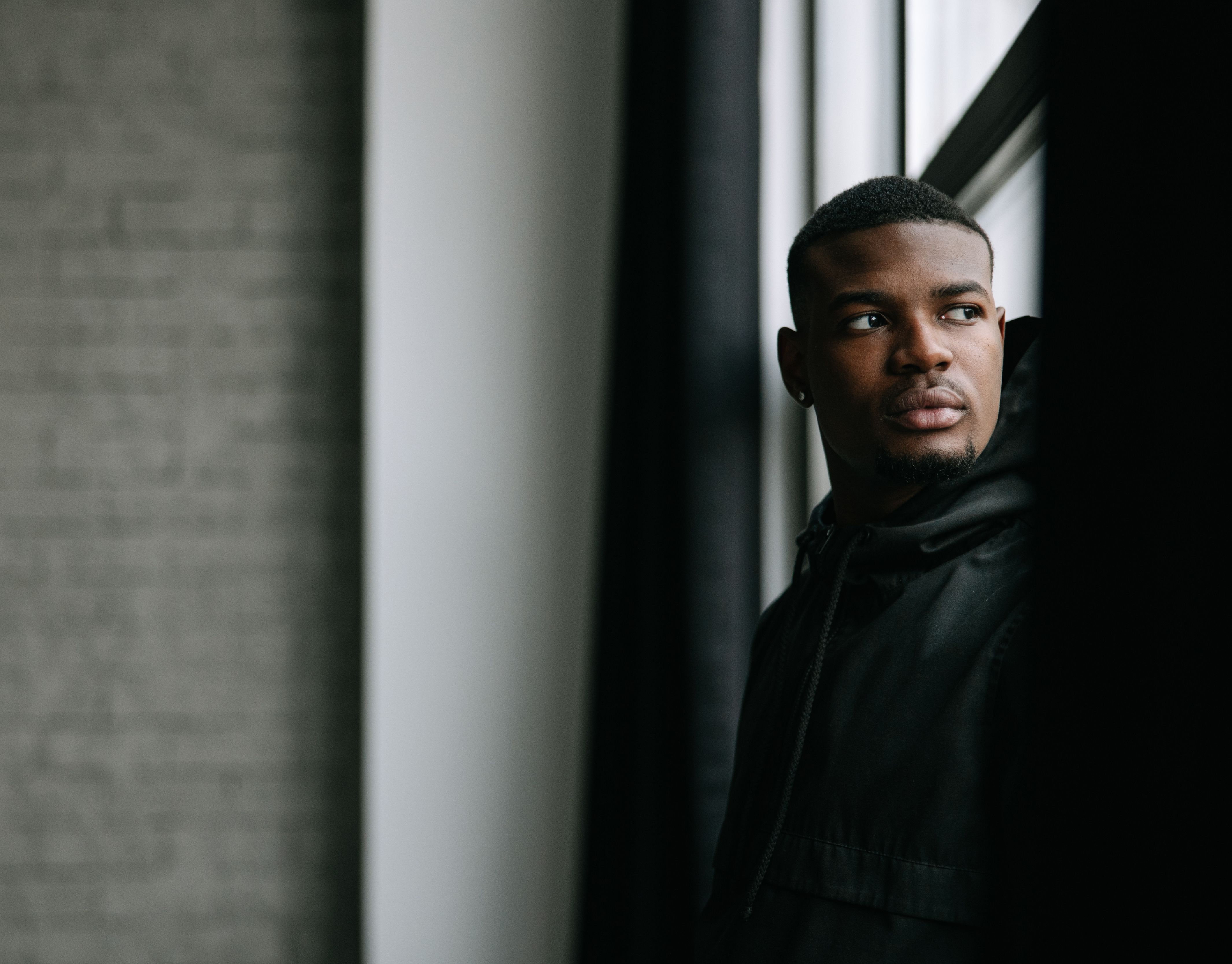 A thoughtful young man gazing outside through natural light indoors.