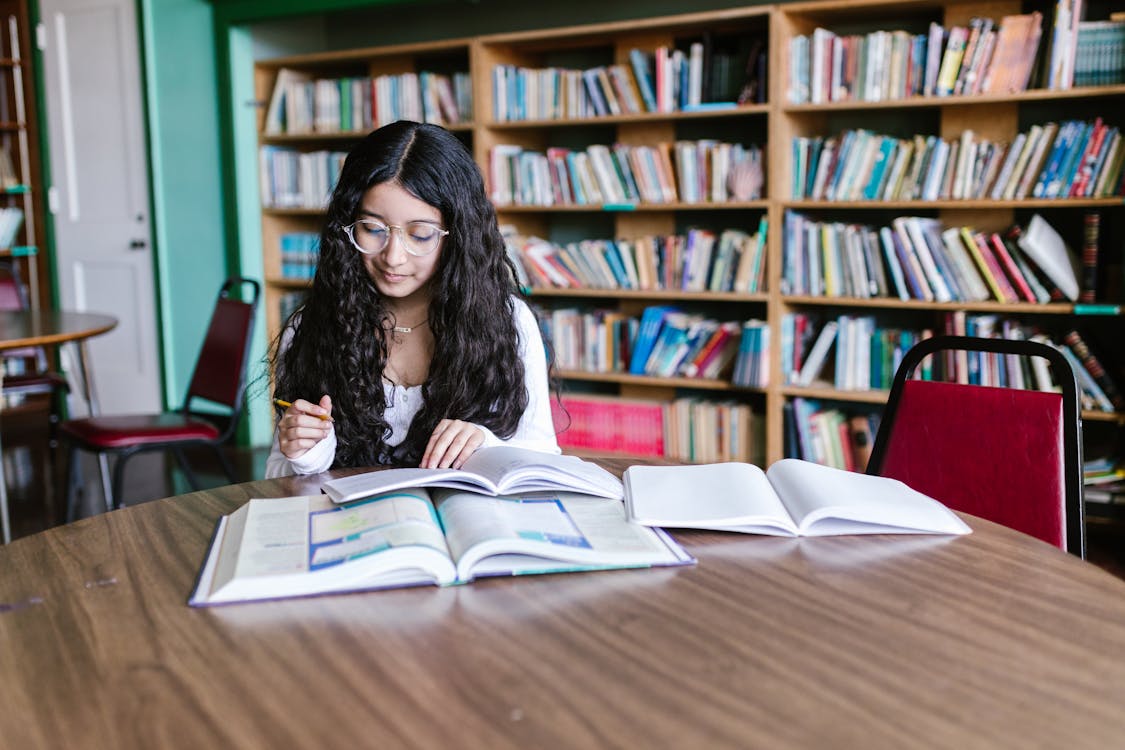 A Girl Reading Book while Sitting on a Chair Inside the Library 