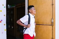 A smiling boy with a backpack entering school, ready for a new academic year.