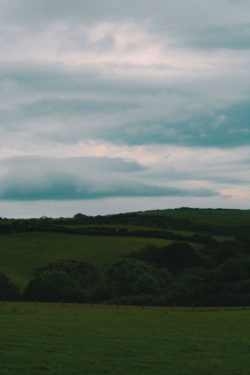 Free A peaceful view of green rolling hills under a cloudy sky, perfect for nature and travel themes. Stock Photo