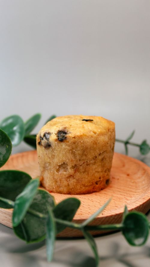 Free A single chocolate chip muffin sits on a wooden plate surrounded by green leaves. Stock Photo