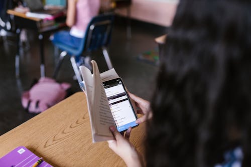 Person Holding Black Mobile Phone while Reading a Book