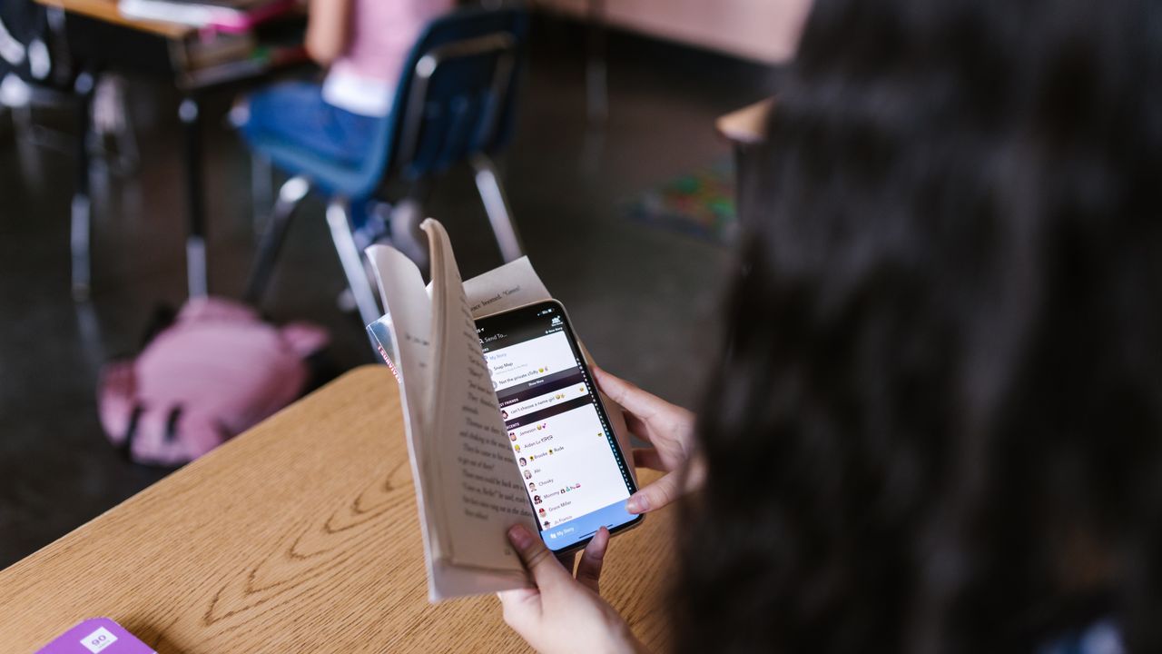Digital distraction while reading Person holding a smartphone while reading a book representing digital distraction and screen time
